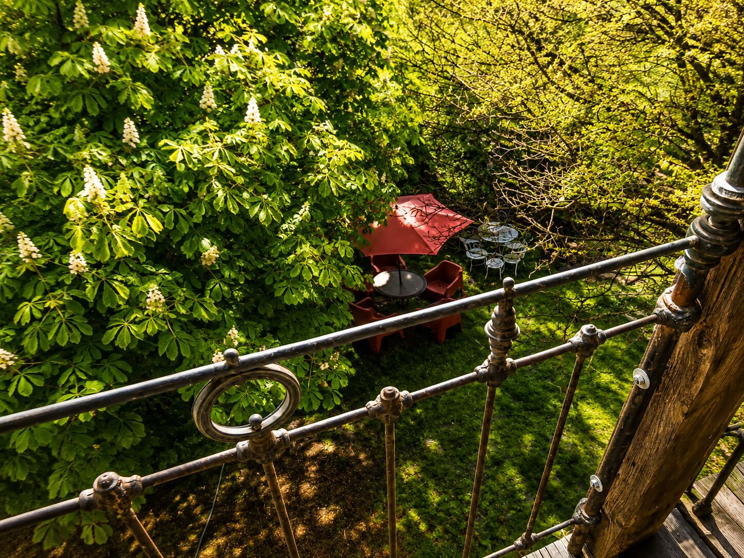 Ein Garten mit einem roten Sonnenschirmtisch und Stühlen, umgeben von üppigem Grün.