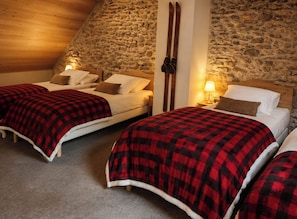 A room with two beds, each with a red and black checkered blanket, wooden headboards, and a stone wall. - L'Alpin, an apartment in the heart of the Domaine de la Grande Longe in Oisans (Le Bourg-d'Oisans)