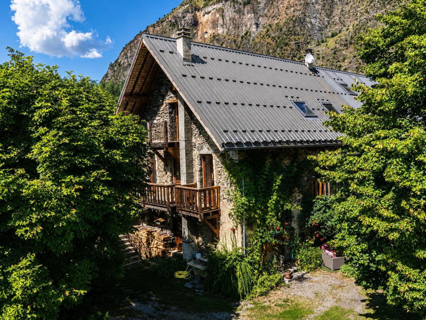 A stone house with a sloped roof, wooden balcony, and a garden area.
