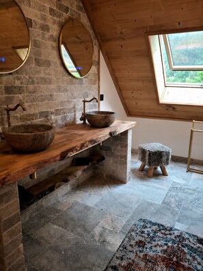 Un baño rústico con lavamanos de piedra, tocador de madera y tragaluz.