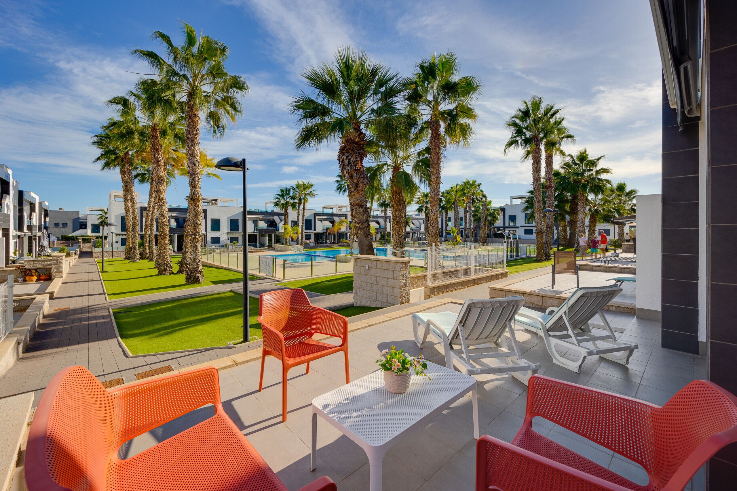 A poolside area with palm trees, lounge chairs, and a clear sky.
