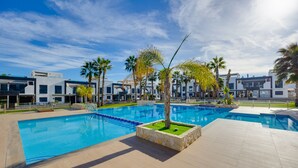 Et moderne hotel med en stor swimmingpool, palmer og moderne arkitektur.