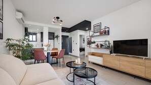 En moderne stue med sofa, spiseplads med stole, fjernsyn og bogreol.