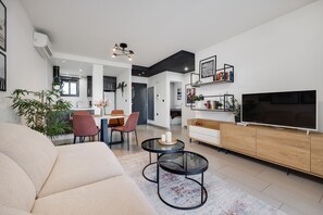 Ein modernes Wohnzimmer mit einer Couch, einem Essbereich mit Stühlen, einem Fernseher und einem Bücherregal.