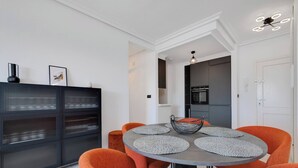 A modern dining area with a round table, orange chairs, and a black cabinet with glass doors. - CB Living - Seaview penhouse in Cabo Roig (Orihuela)