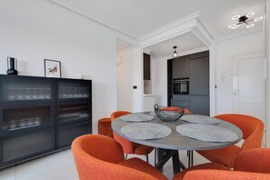 A modern dining area with a round table, orange chairs, and a black cabinet with glass doors. - CB Living - Seaview penhouse in Cabo Roig (Orihuela)