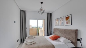 A hotel room with a bed, a nightstand, a lamp, and a view of the outdoors. - CB Living - Seaview penhouse in Cabo Roig (Orihuela)