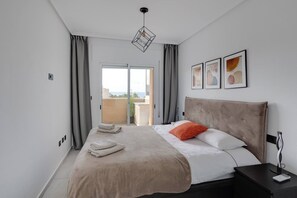 A hotel room with a bed, a nightstand, a lamp, and a view of the outdoors. - CB Living - Seaview penhouse in Cabo Roig (Orihuela)