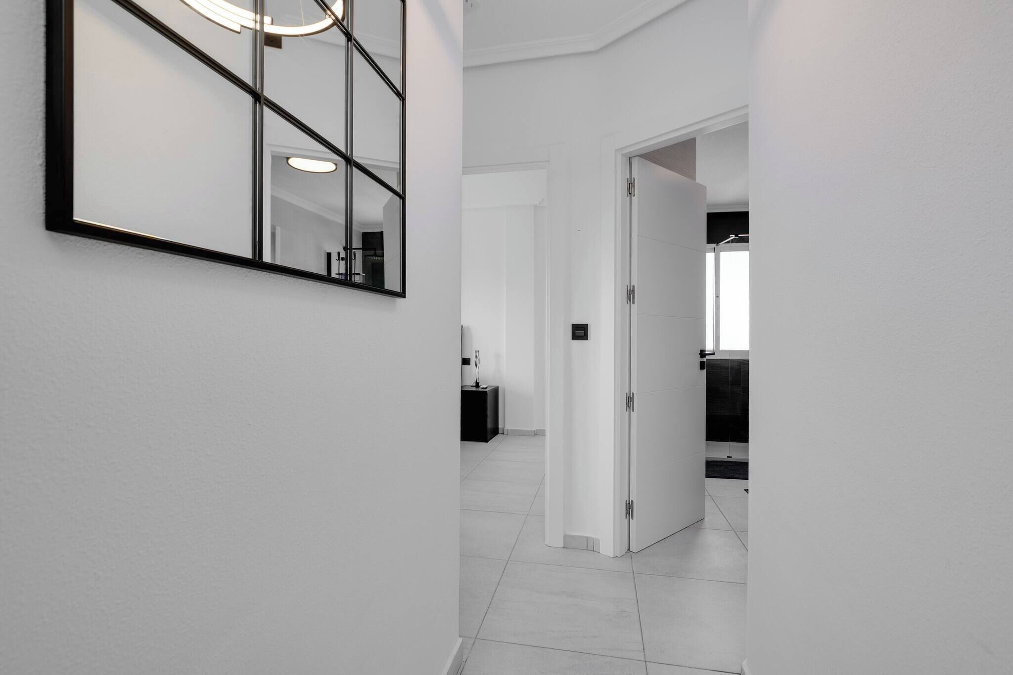 A hallway with a large mirror, a door leading to a bathroom, and a tiled floor.
