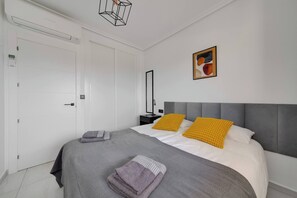 A modern bedroom with a grey upholstered bed, two pillows, a bedside table, a wall-mounted lamp, and a framed abstract painting. - CB Living - Seaview penhouse in Cabo Roig (Orihuela)