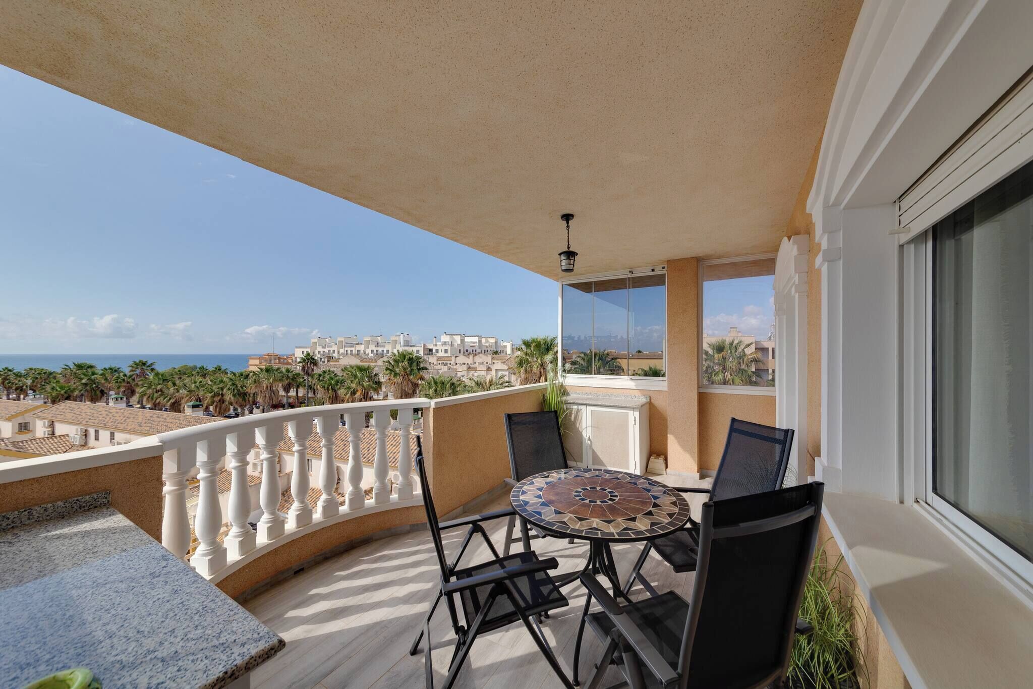 A balcony with a table and chairs, overlooking a coastal cityscape.