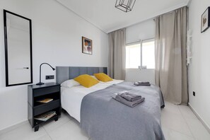Une chambre à coucher moderne, avec un lit, des tables de chevet, une commode, une fenêtre avec des rideaux et un tableau accroché au mur.