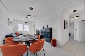 A modern living space with a dining area, a sofa, a television, and a kitchen area. - CB Living - Seaview penhouse in Cabo Roig (Orihuela)