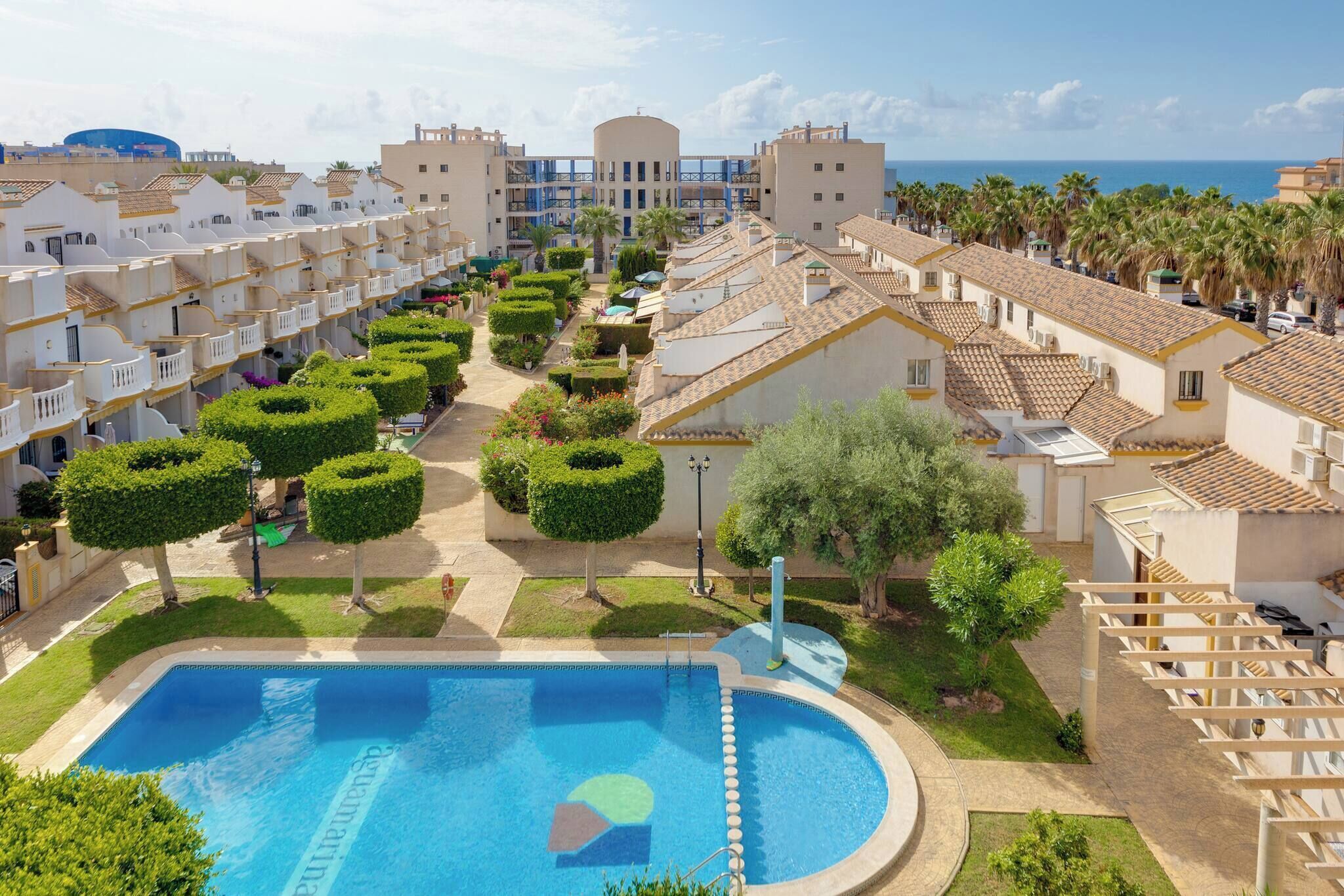 A resort with a swimming pool, well-maintained gardens, and a view of the sea.