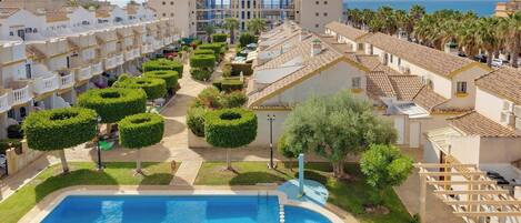 A resort with a swimming pool, well-maintained gardens, and a view of the sea.