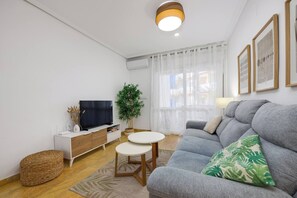 A modern living room with a sofa, a television, a small table, and a plant. - CB Living- Beachfront apartment Aquamarina (Orihuela)