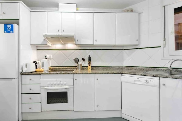 A kitchen with white cabinets, a built-in oven, a dishwasher, and a coffee maker.