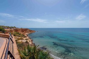 A coastal landscape with a clear view of the sea, a paved walkway, and a rocky cliff. - CB Living- Beachfront apartment Aquamarina (Orihuela)