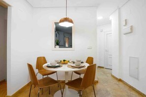 A dining area with a round table, four chairs, a hanging light fixture, and a mirror on the wall. - CB Living- Beachfront apartment Aquamarina (Orihuela)