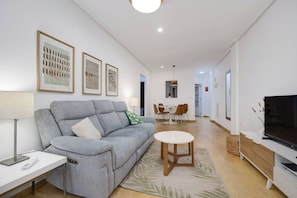 A modern living room with a grey sofa, a round coffee table, and a flat-screen TV on a wooden TV stand.