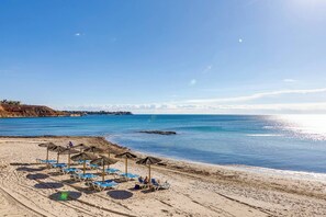 A beach with lounge chairs and umbrellas, a clear sky, and calm sea.