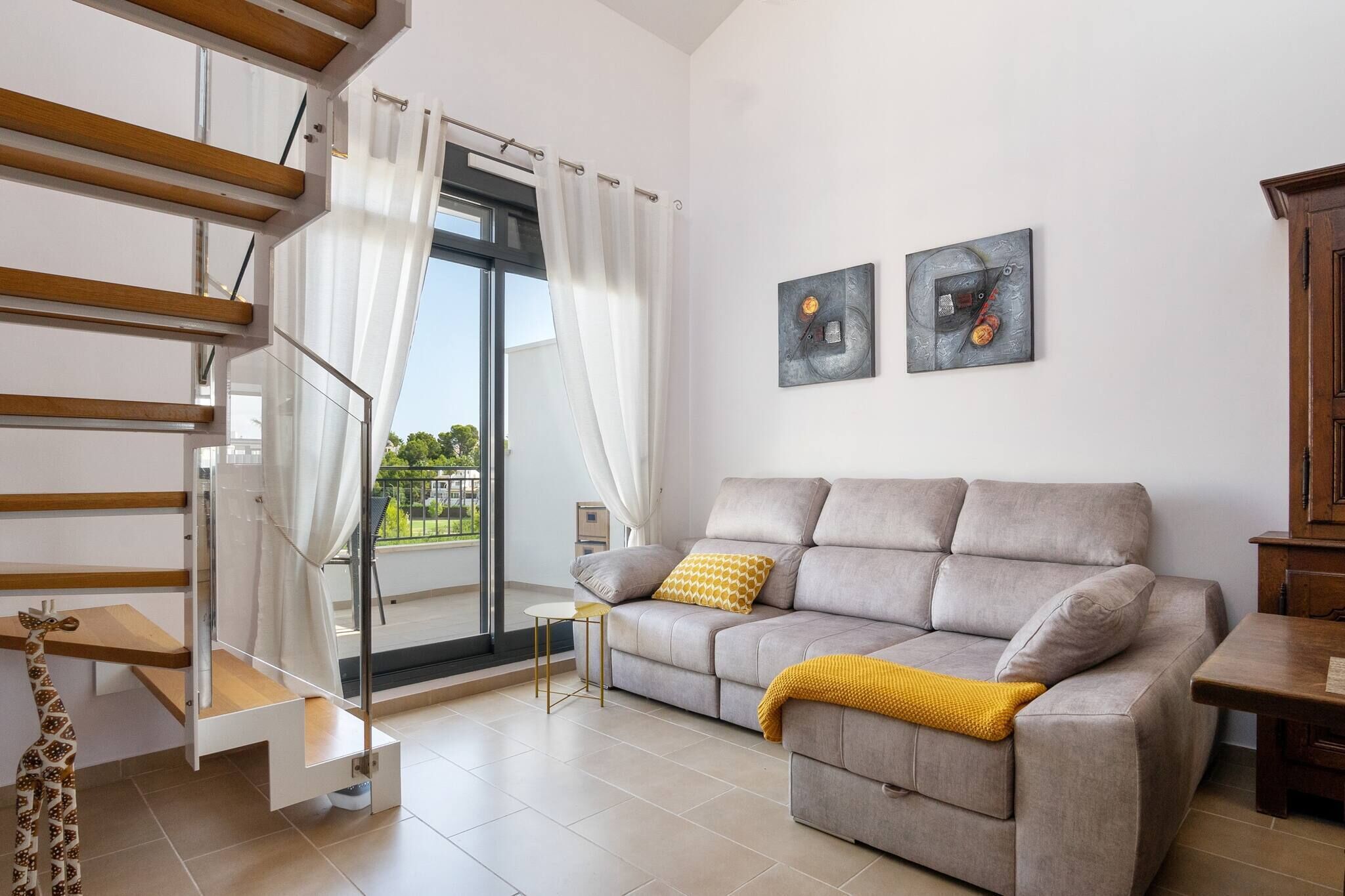 Uma sala de estar moderna com um sofá cinzento, um cobertor amarelo e uma escada com grades de madeira.