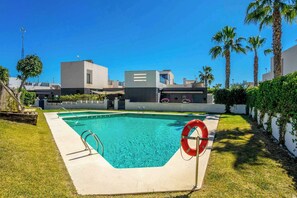 A swimming pool with a lifebuoy, surrounded by a grassy area and palm trees. - CB Living - Cosy loft with terrace, Villamartin (Orihuela)