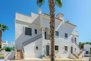 A two-story building with a staircase leading to the entrance, a balcony, and a palm tree in the foreground. - CB Living - Cosy loft with terrace, Villamartin (Orihuela)