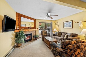 Ein Wohnzimmer mit Kamin, Wand-Fernseher, Deckenventilator und großem Fenster.