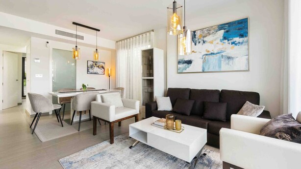 A modern living room with a white sofa, a coffee table, and a dining area with chairs and a table. - CB Living - 3 bedroom home in Punta Prima (Alicante / Alacant)