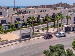 Ein Wohngebiet mit modernen Gebäuden, eine Straße mit Autos und im Hintergrund ein freier Blick auf das Meer.