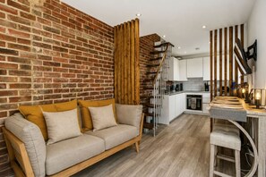 A modern living space with a brick wall, a wooden staircase, a kitchen area, and a seating area with a sofa. - Cosy London Studio Free Parking Sleeps 3 (Morden)