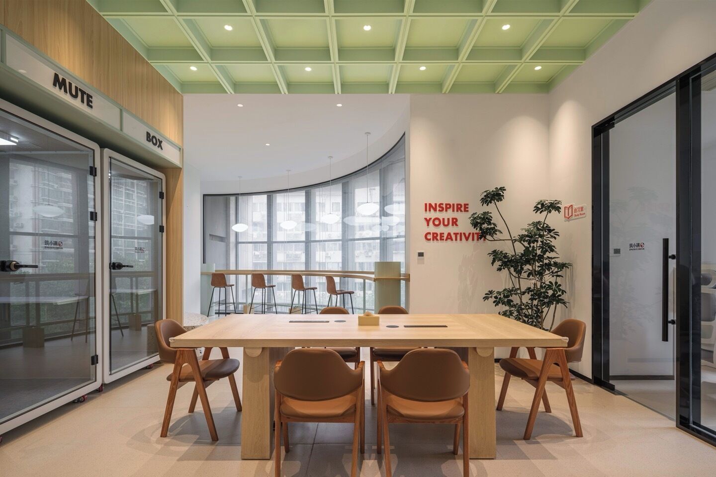 Un moderno salón de conferencias con una amplia mesa, sillas y un separador de vidrio con un letrero que dice 'MUTE'.