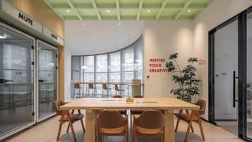 Un moderno salón de conferencias con una amplia mesa, sillas y un separador de vidrio con un letrero que dice 'MUTE'.
