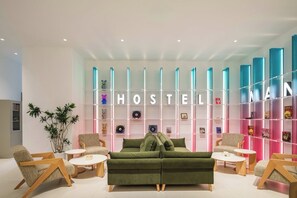Uma área de estar moderna com um sofá verde, cadeiras de madeira e uma estante com livros e objetos decorativos.