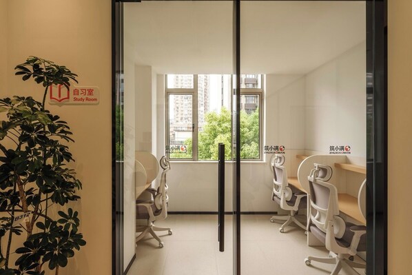 Une salle d’étude équipée de deux chaises, d’un bureau, d’une grande fenêtre et d’une plante.