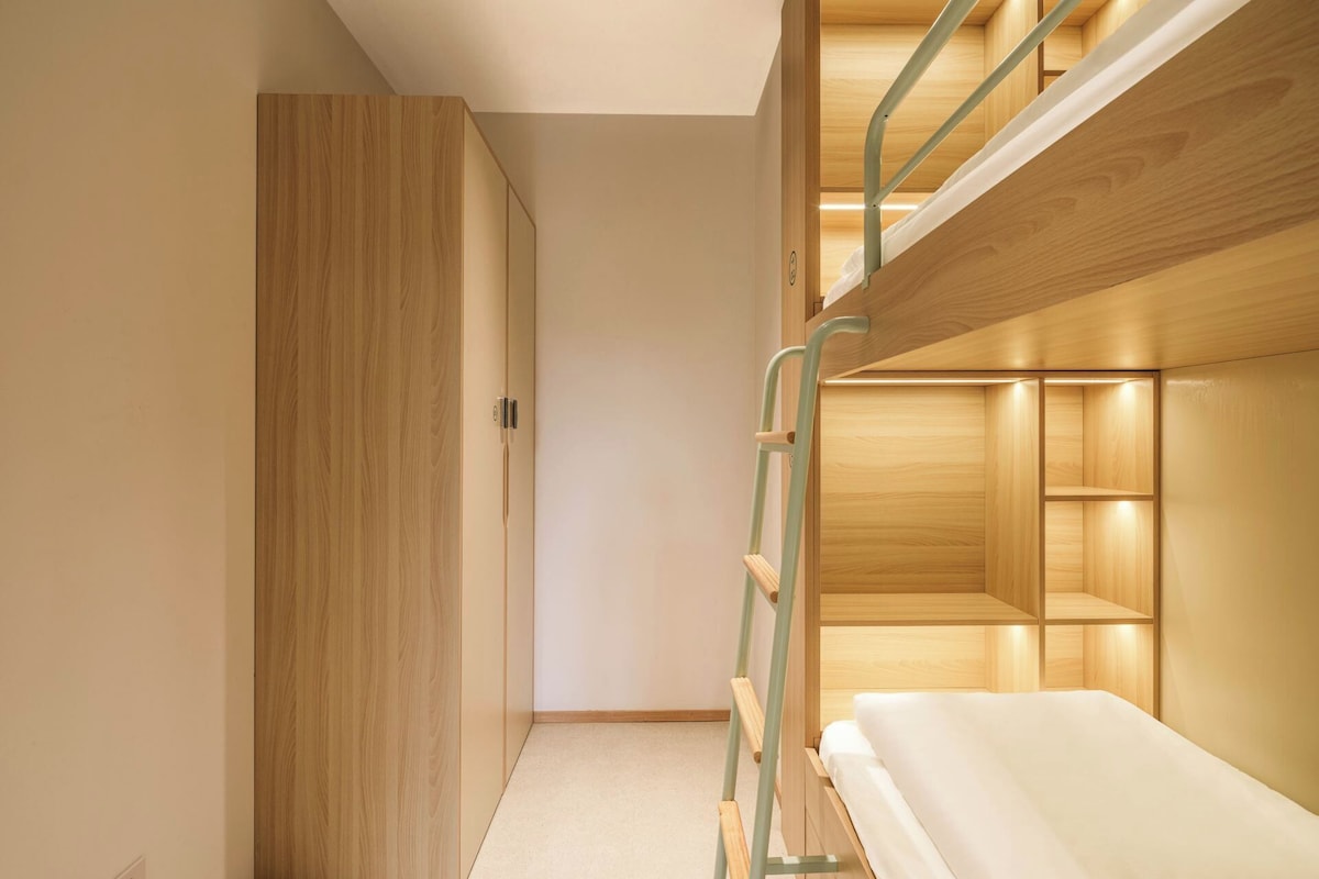 A bunk bed with a ladder, a wardrobe, and a small bedside table.
