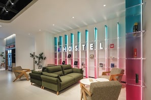 A modern hostel interior with a green sofa, two armchairs, a coffee table, and a bookshelf with various items. - Shanghai Zhuxiaoman Urban Hostel (Shanghai)
