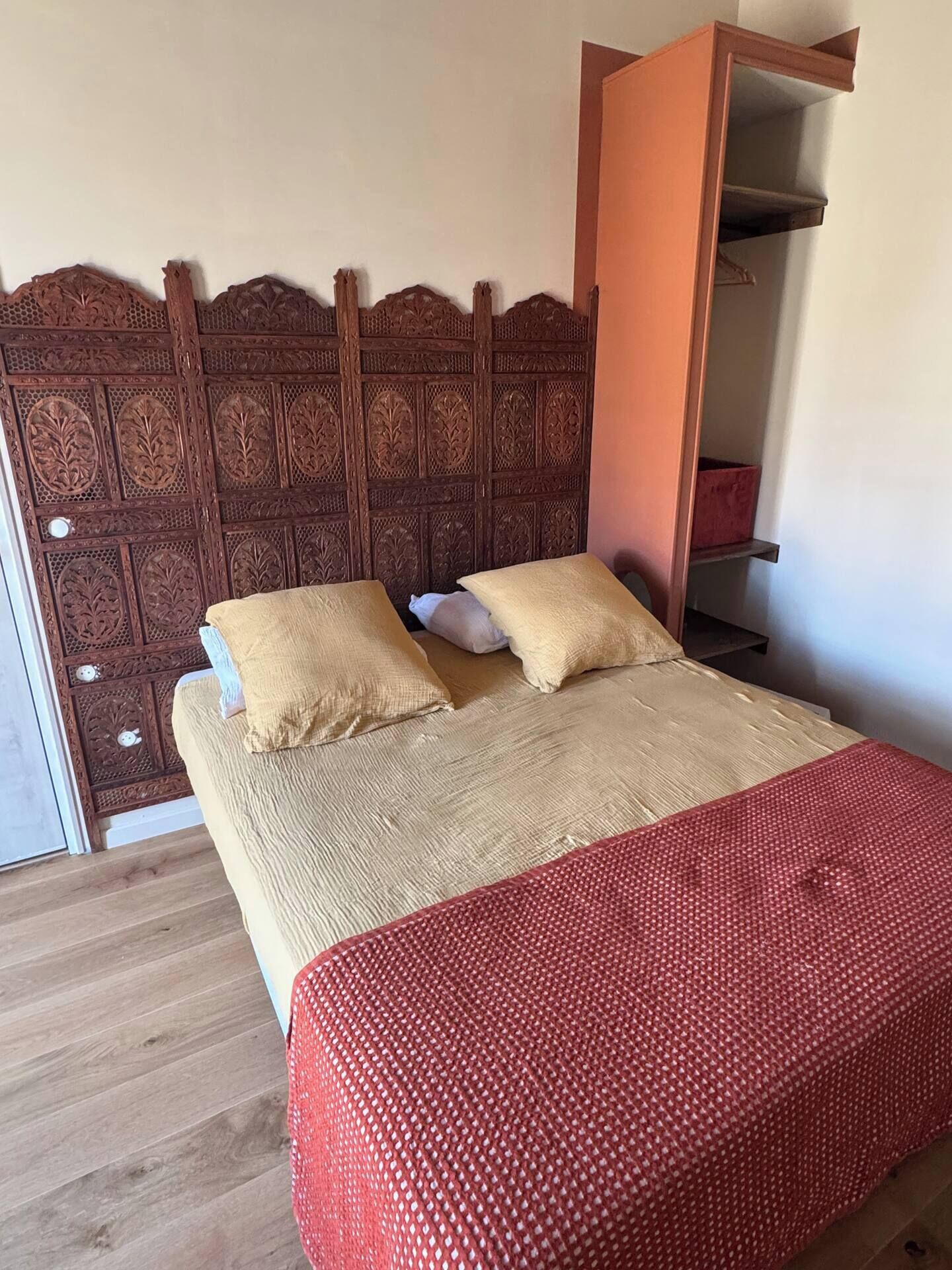 A bed with a wooden headboard, two pillows, and a red blanket.
