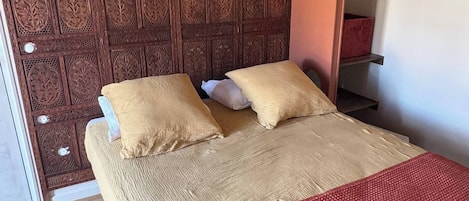 A bed with a wooden headboard, two pillows, and a red blanket.