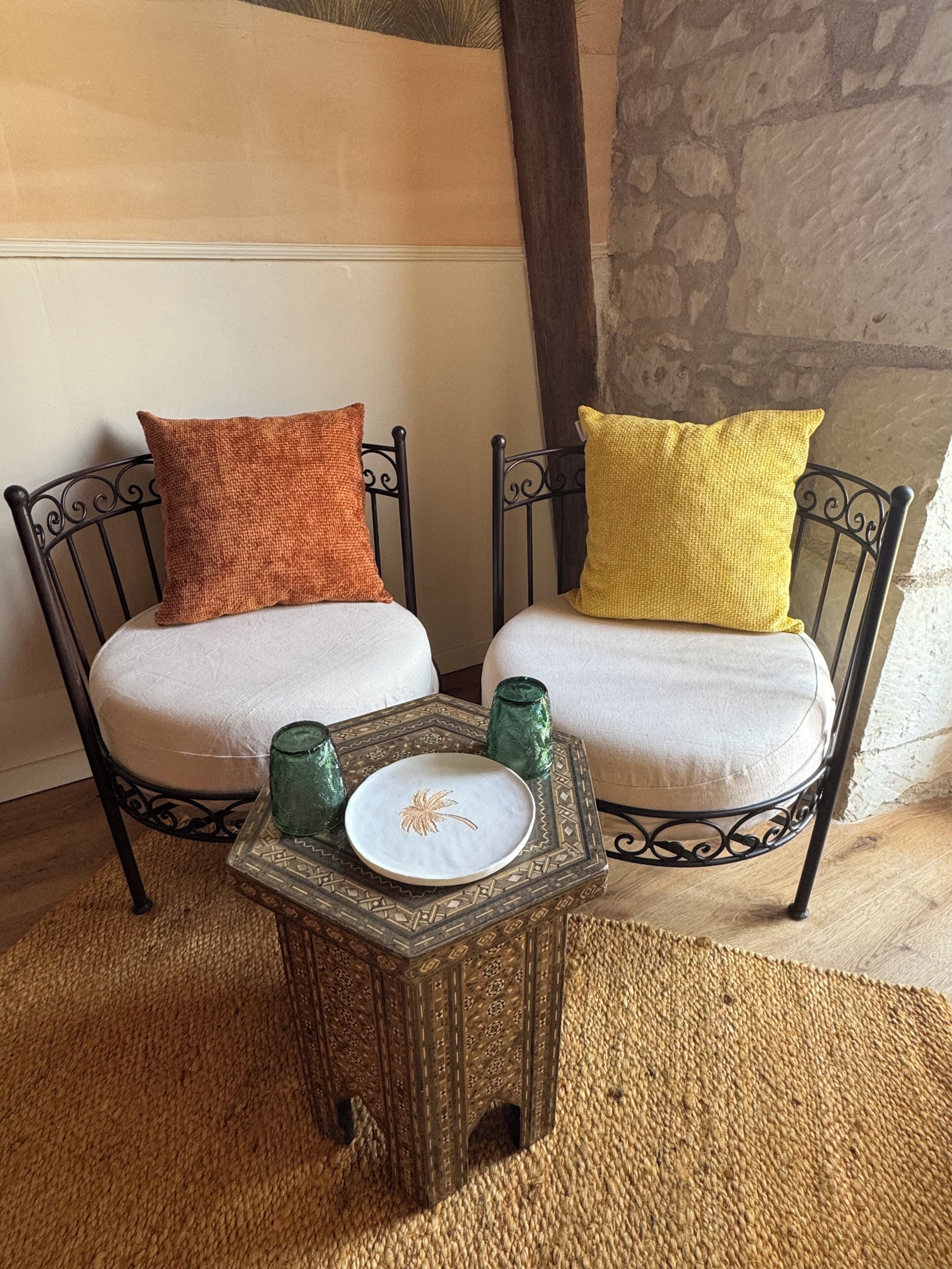 Two chairs with cushions, a small table with a plate, and two green vases.