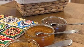 Une table en bois avec trois pots de confiture, une cuillère et un panier de pain.