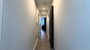 A narrow hallway with a wooden floor, white walls, and a radiator on the right. - Modern one bedroom apartment in Richmond upon Thames (London)