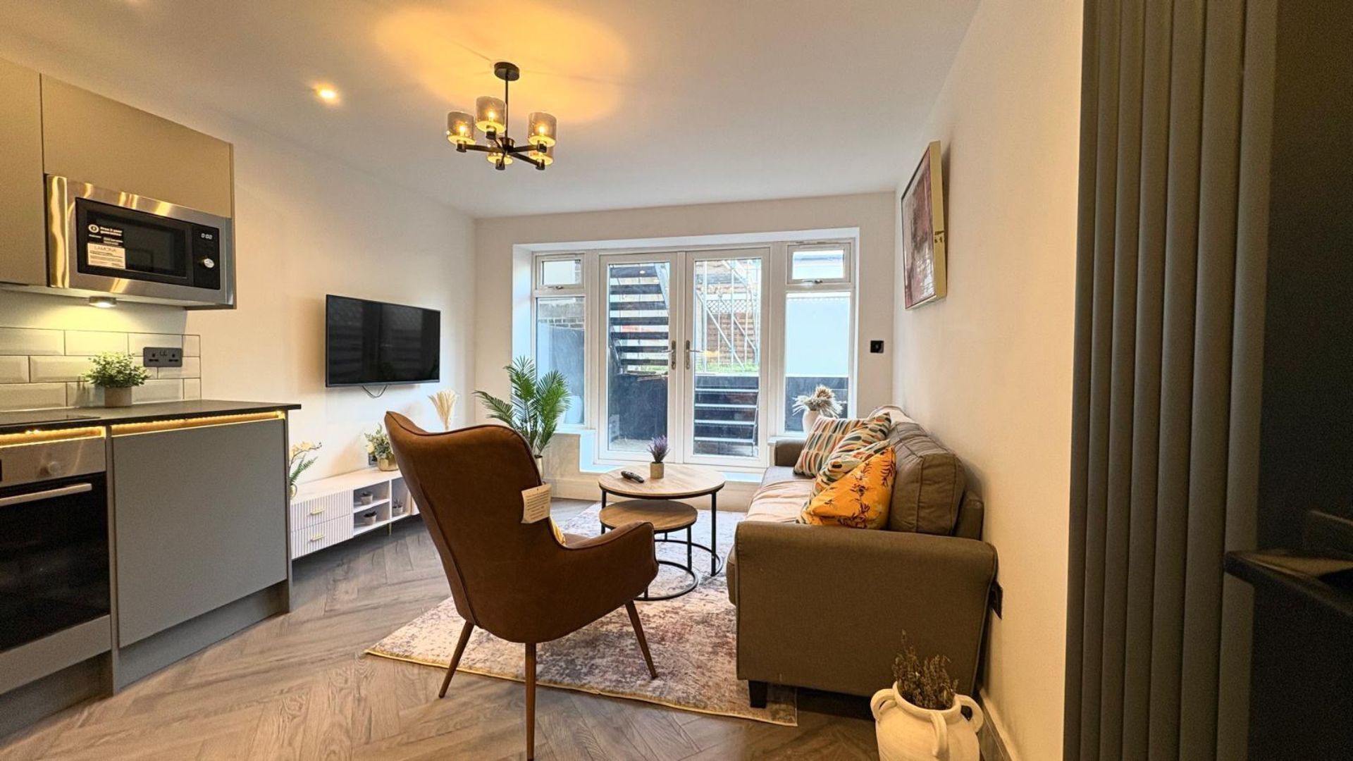 A modern kitchen with a built-in microwave, a dining area with a round table and chairs, and a living room with a sofa and a TV.