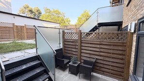 A patio area with a wooden fence, outdoor furniture, and a staircase leading to an upper level. - Modern one bedroom apartment in Richmond upon Thames (London)