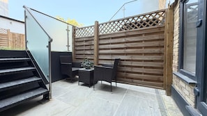A patio area with a wooden fence, outdoor furniture, and a staircase leading to an upper level. - Modern one bedroom apartment in Richmond upon Thames (London)