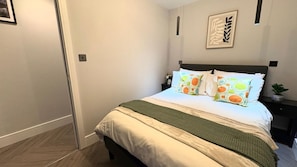 A bedroom with a bed, pillows, a nightstand, a wall art piece, and a door. - Modern one bedroom apartment in Richmond upon Thames (London)
