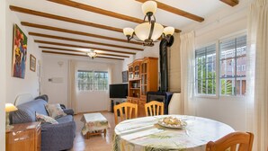 Ein Wohnzimmer mit einer Couch, einem Esstisch mit Stühlen, einem Fernseher und einem Bücherregal.