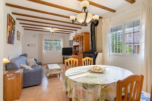 A living room with a sofa, a dining table with chairs, a television, and a bookshelf. - Bungalow 'Magnifico Chalet Con Piscina' with Shared Pool, Wi-Fi and Air Conditioning (Gran Alacant)