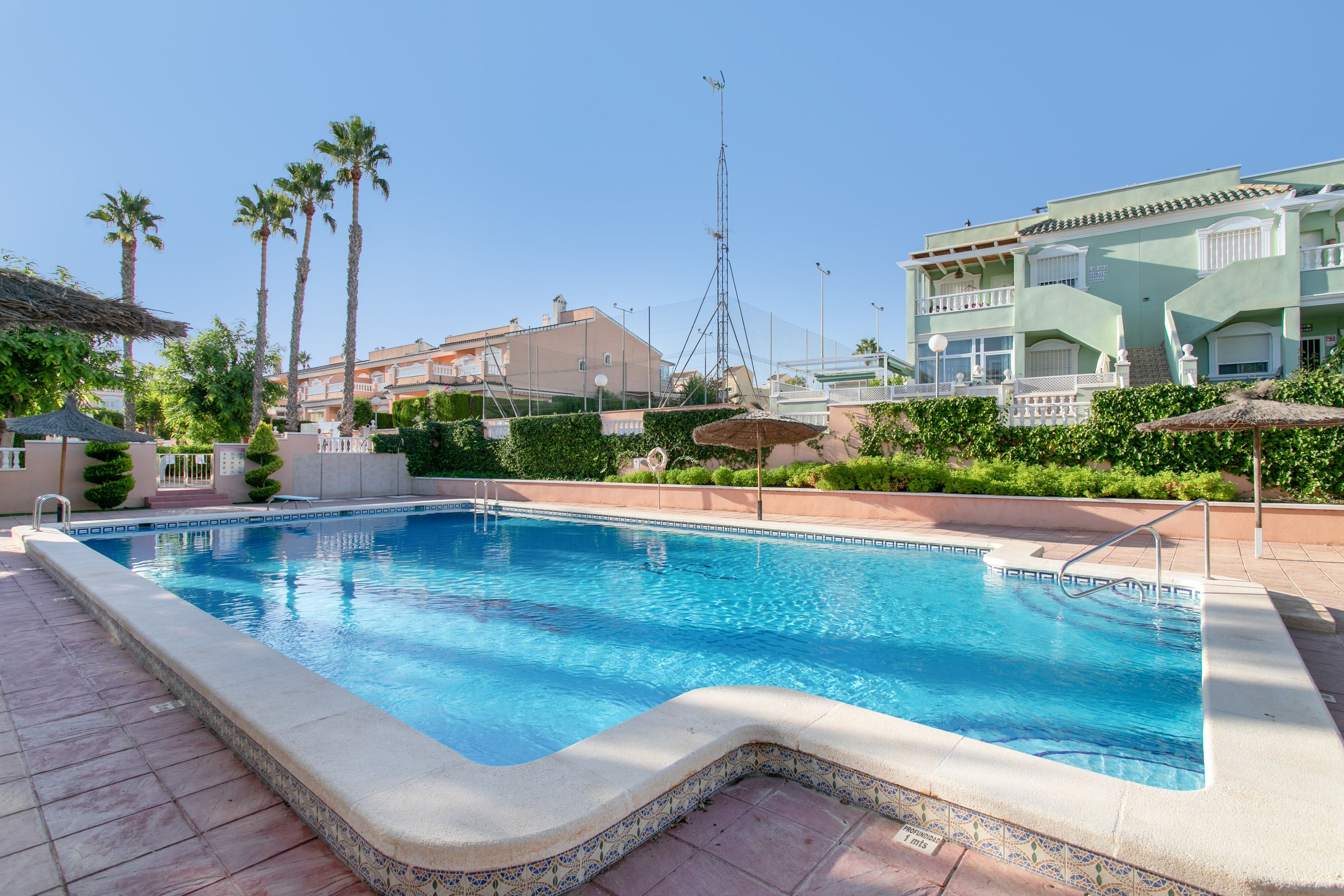 Ein Pool mit einer gefliesten Kante, umgeben von Palmen und einem Gebäude mit einem Balkon.